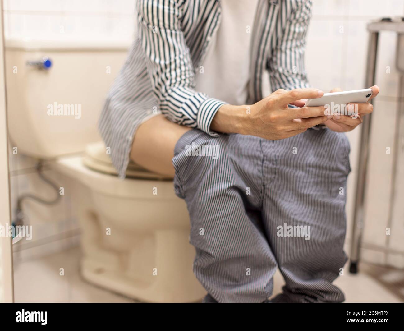 Der Mann hat Durchfall in der Toilette und nutzt das Mobiltelefon horizontal, um Handyspiele zu spielen/Videos auf dem Mobiltelefon anzusehen Stockfoto