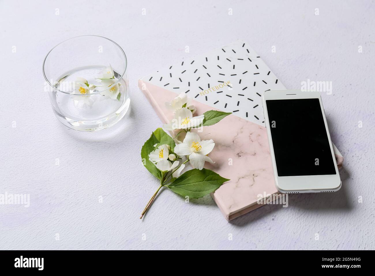 Handy, Notebook, Jasminblüten und Glas Wasser auf hellem Hintergrund Stockfoto