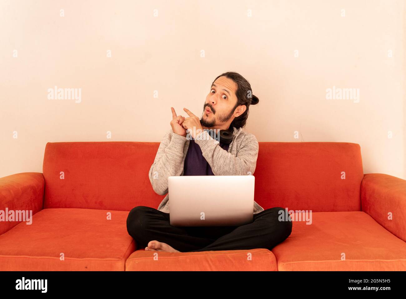 Der junge Mann zeigt mit dem Finger auf einem orangefarbenen Sofa im Wohnzimmer zu Hause. Konzept für Verkaufszeit. Stockfoto