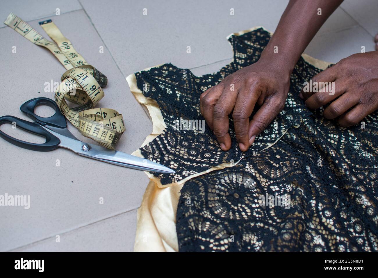 Ein afrikanischer Modedesigner reicht die Hände, die an einem Kleid, Stoff oder einer Kleidung mit einem Maßband und einer Schere arbeiten, um die beste Leistung als Schneider zu erhalten Stockfoto