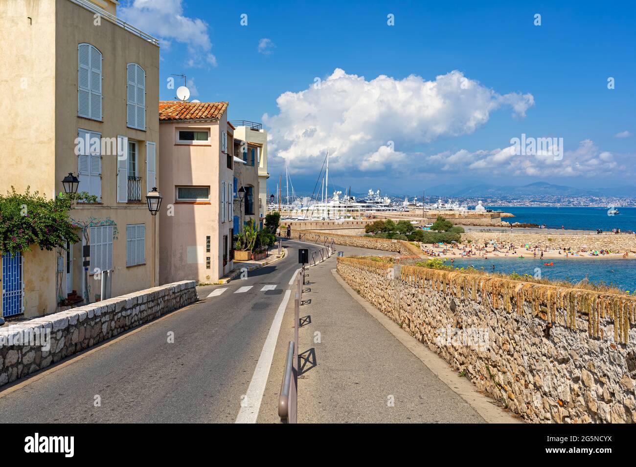 Fußgängerweg und schmale Stadtstraße entlang der Häuser und der Mittelmeerküste unter blauem Himmel in Antibes - Stadt an der Französischen Riviera. Stockfoto