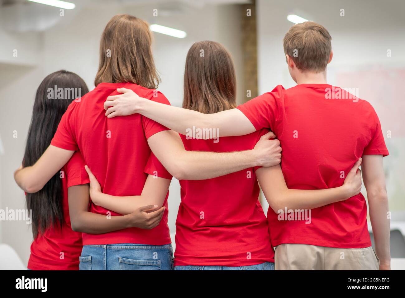 Freiwillige umarmen sich stehend mit dem Rücken zur Kamera Stockfoto