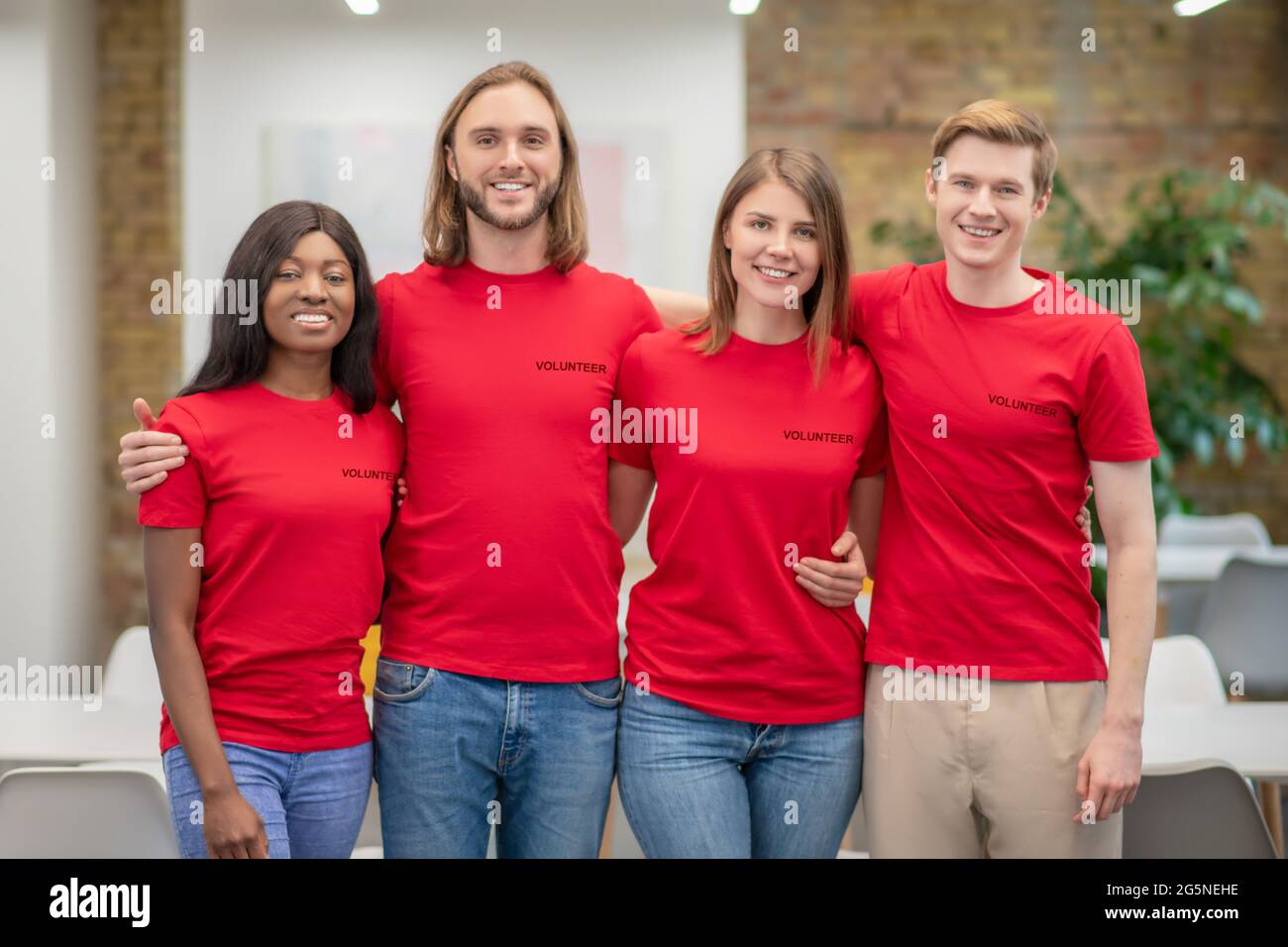 Gruppe lächelnder junger Freiwilliger, die umarmt stehen Stockfoto