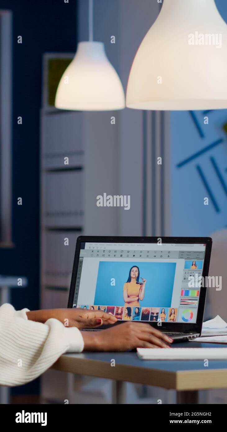 Dunkelhäutiger Freiberufler Retuscherin Frau, die Überstunden am Laptop mit Fotobearbeitungssoftware arbeitet. Professioneller Grafikeditor Retusche Foto eines Kunden in der Nacht im Home Office auf Performance-pc Stockfoto