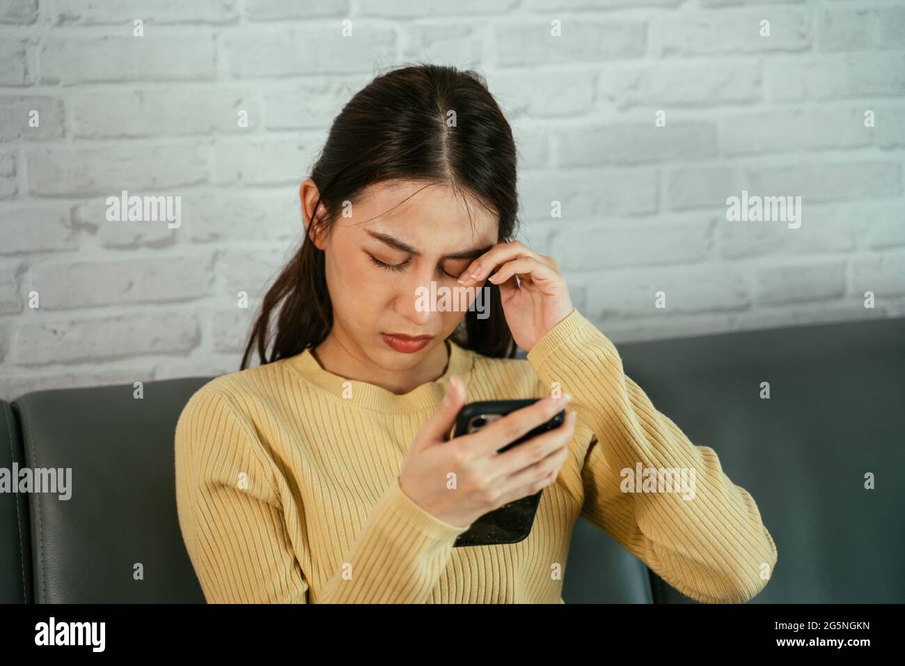 Junge asiatische Frau, die sich die Augen reibt, weil sie das Gefühl der Unannehmlichkeit hat, das Smartphone stundenlang ohne Pause und Pause zu Hause zu benutzen Stockfoto