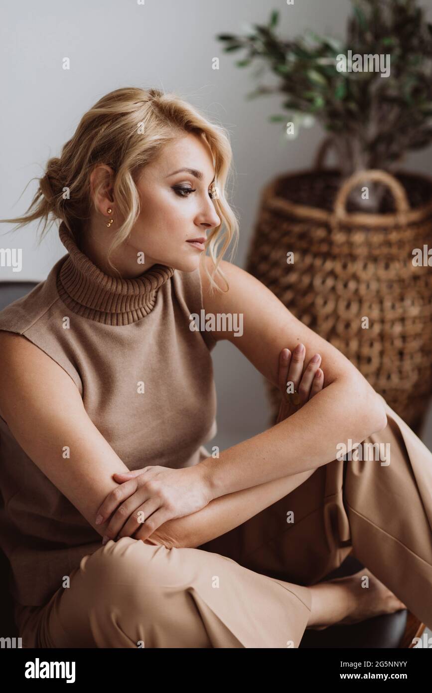 Schöne nachdenkliche Frau entspannt sich in einem modernen Loft-Interieur. Frau in beigefarbener Freizeitkleidung. Weicher, selektiver Fokus. Stockfoto