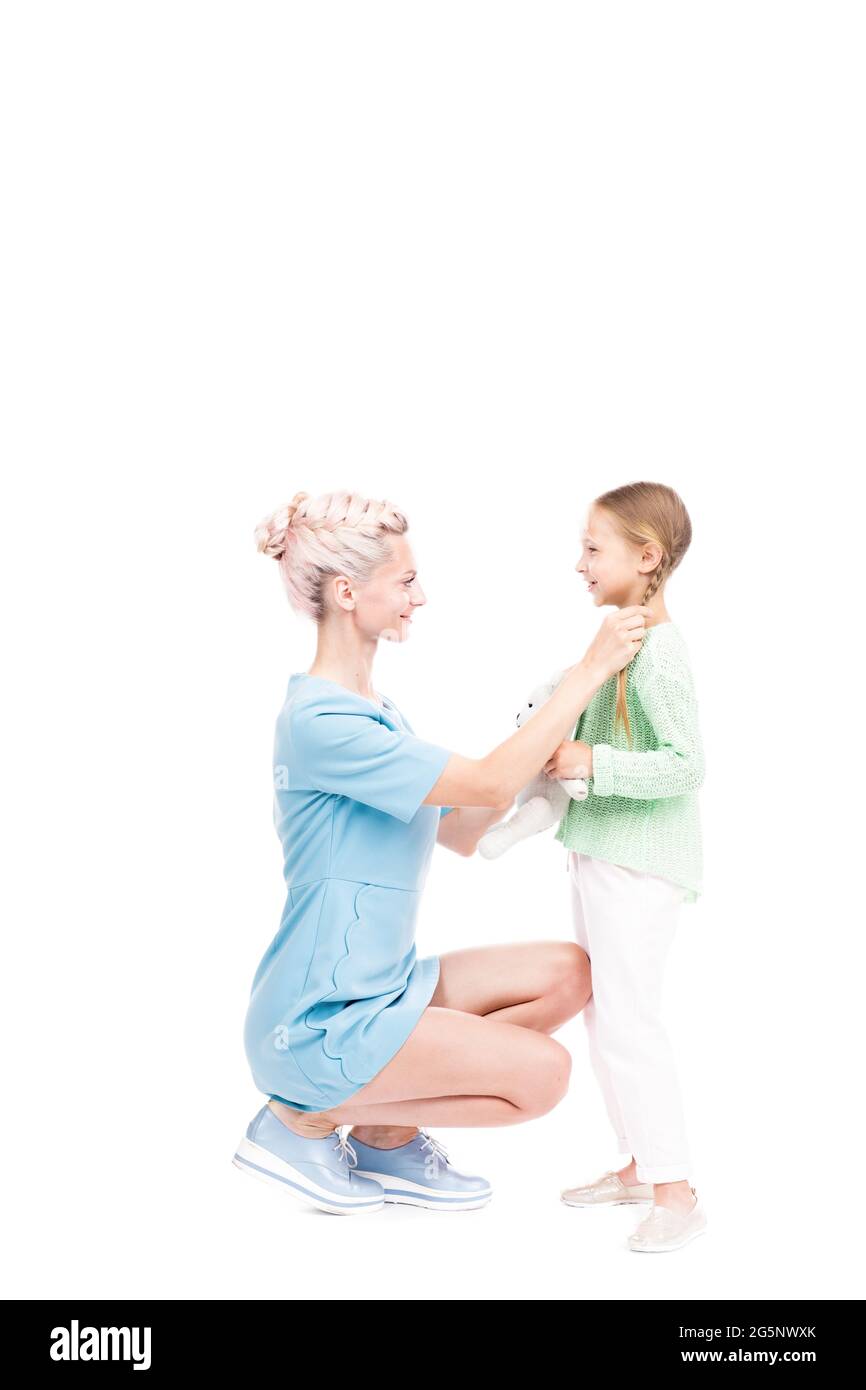 Vertikale Ganzlänge isoliert Aufnahme der modernen Mutter sitzt vor ihrer Tochter Fixierung ihre Haare, weißer Hintergrund Stockfoto
