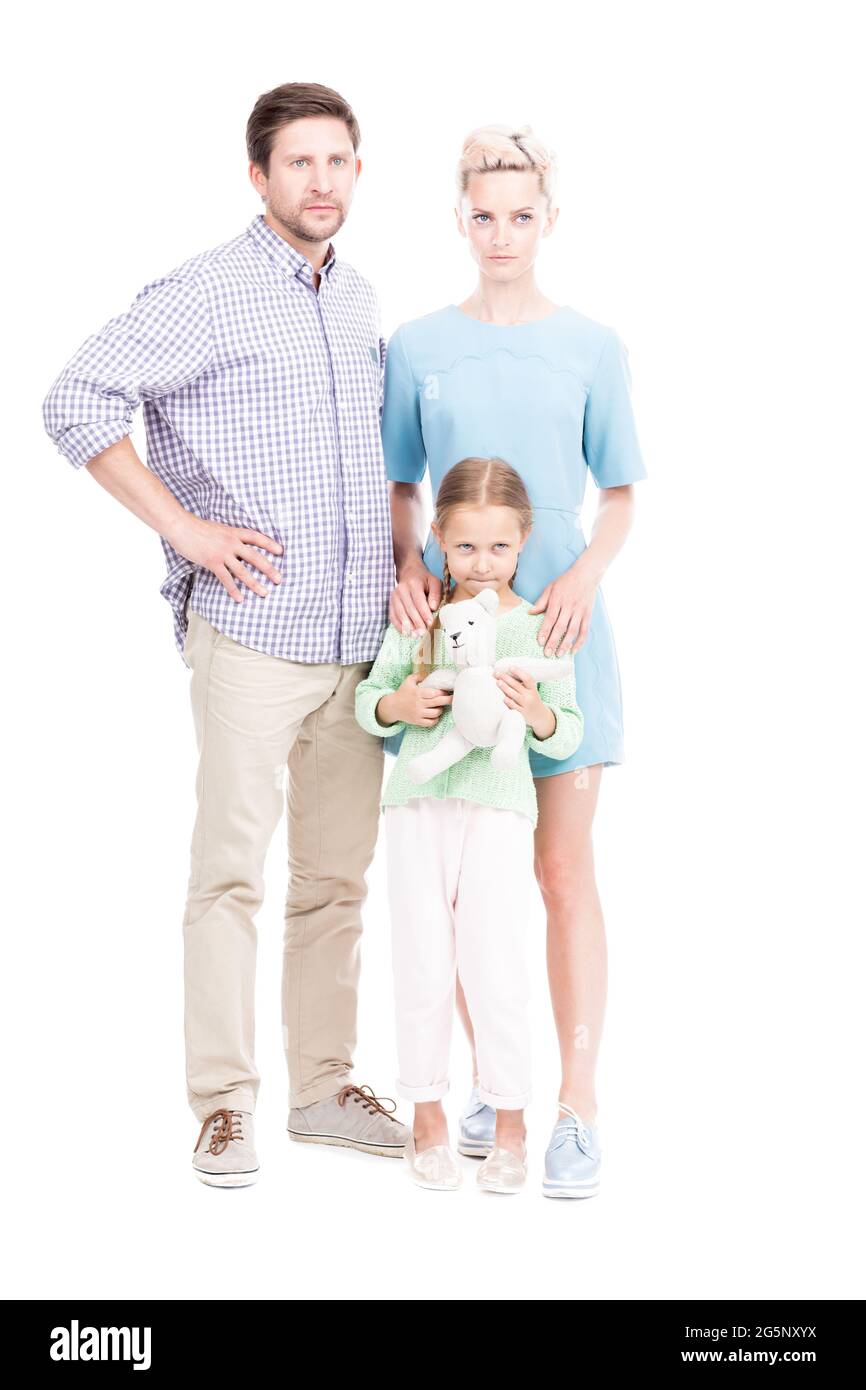 Vertikale, ganzjährige, isolierte Aufnahme der Familie mit einem Kind, das zusammen steht und die Kamera mit ernsthaftem Gesichtsausdruck und weißem Hintergrund anschaut Stockfoto