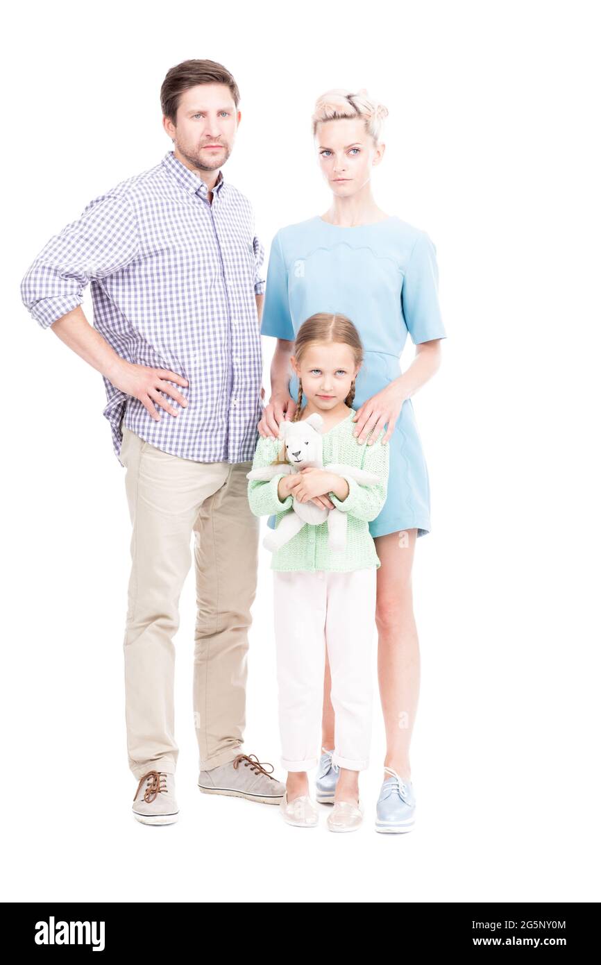 Vertikale, ganzjährige, isolierte Aufnahme der Familie mit einem Kind, das zusammen steht und die Kamera mit ernsthaftem Gesichtsausdruck und weißem Hintergrund anschaut Stockfoto
