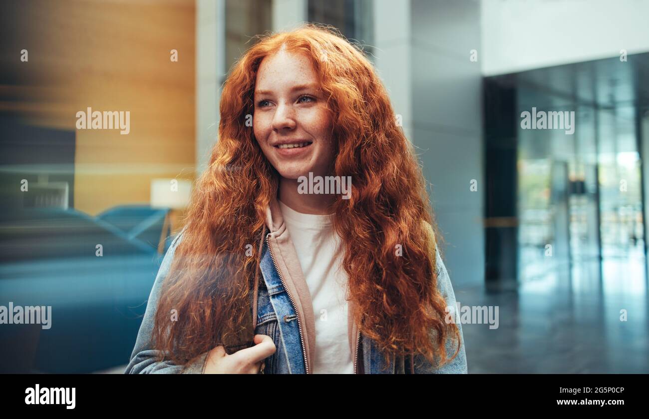 Lässig gekleidete Studentin auf dem Universitätscampus. Junge Frau auf dem College-Campus mit gefärbten roten Haaren. Stockfoto