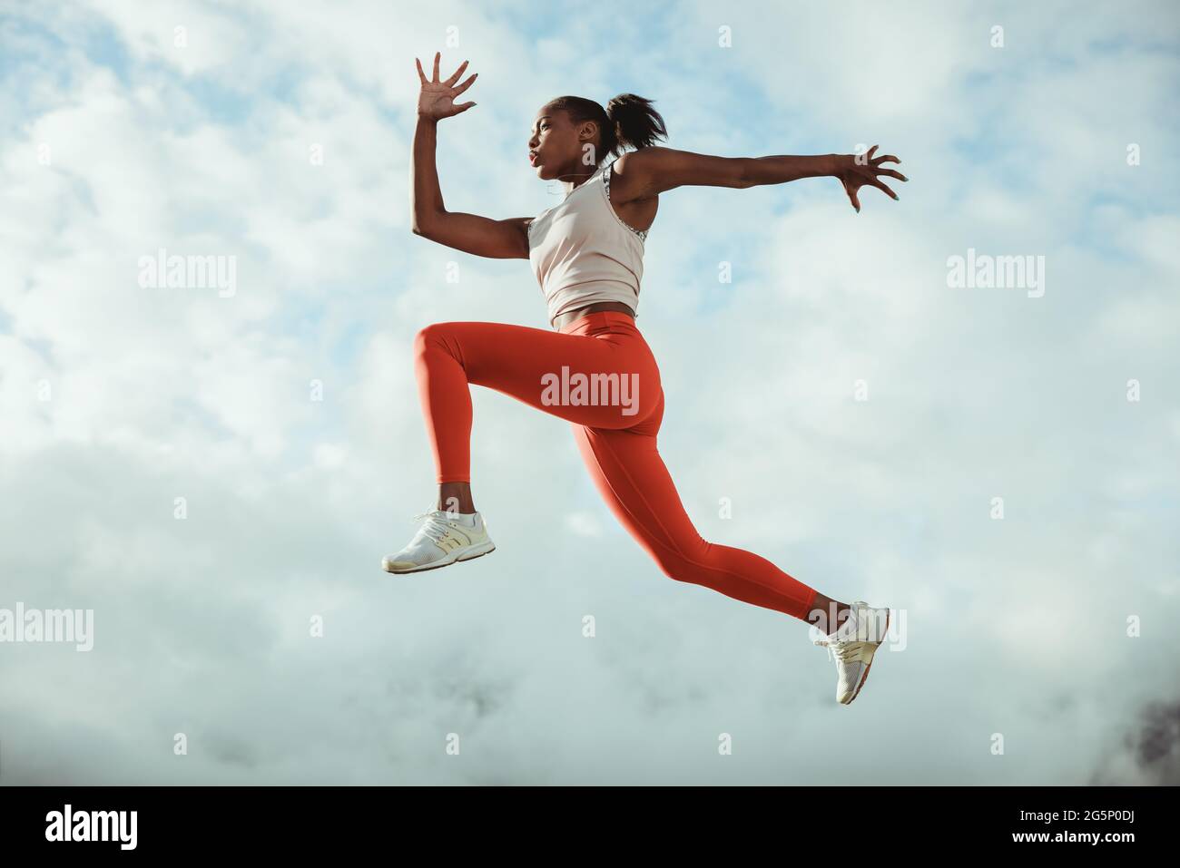 Frau in Sportbekleidung, die im Freien Sprungtraining macht. Fitness-Frau, die in der Luft gegen den Himmel läuft und springt. Stockfoto