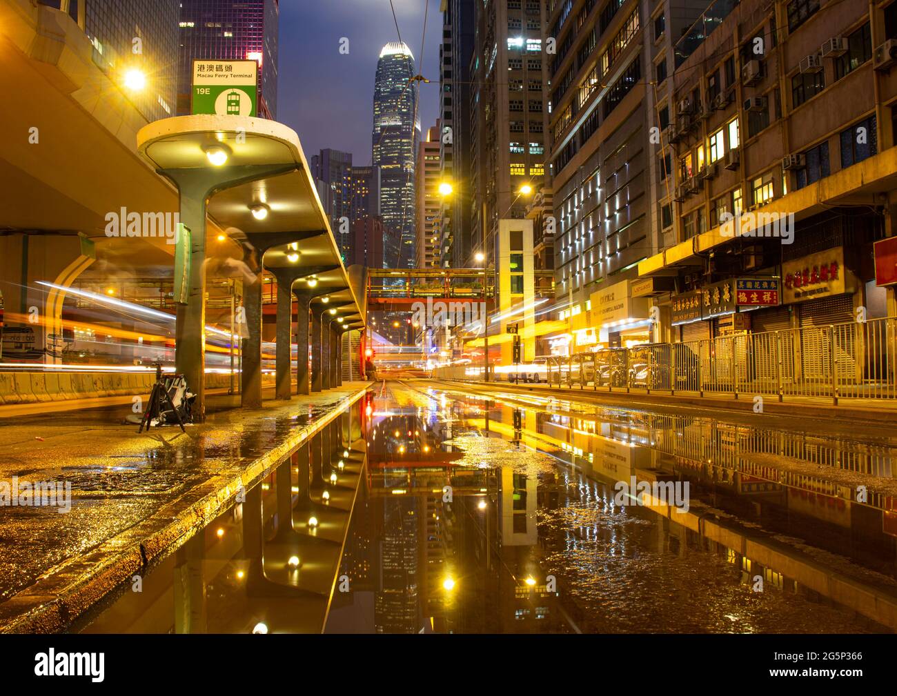 Schöne Farben und Reflexionen an einer Straßenbahnhaltestelle in Hongkong nach einem Sturm. Die lange Belichtung in der Nacht führte zu Lichtstreifen von Bussen und Straßenbahnen. Stockfoto