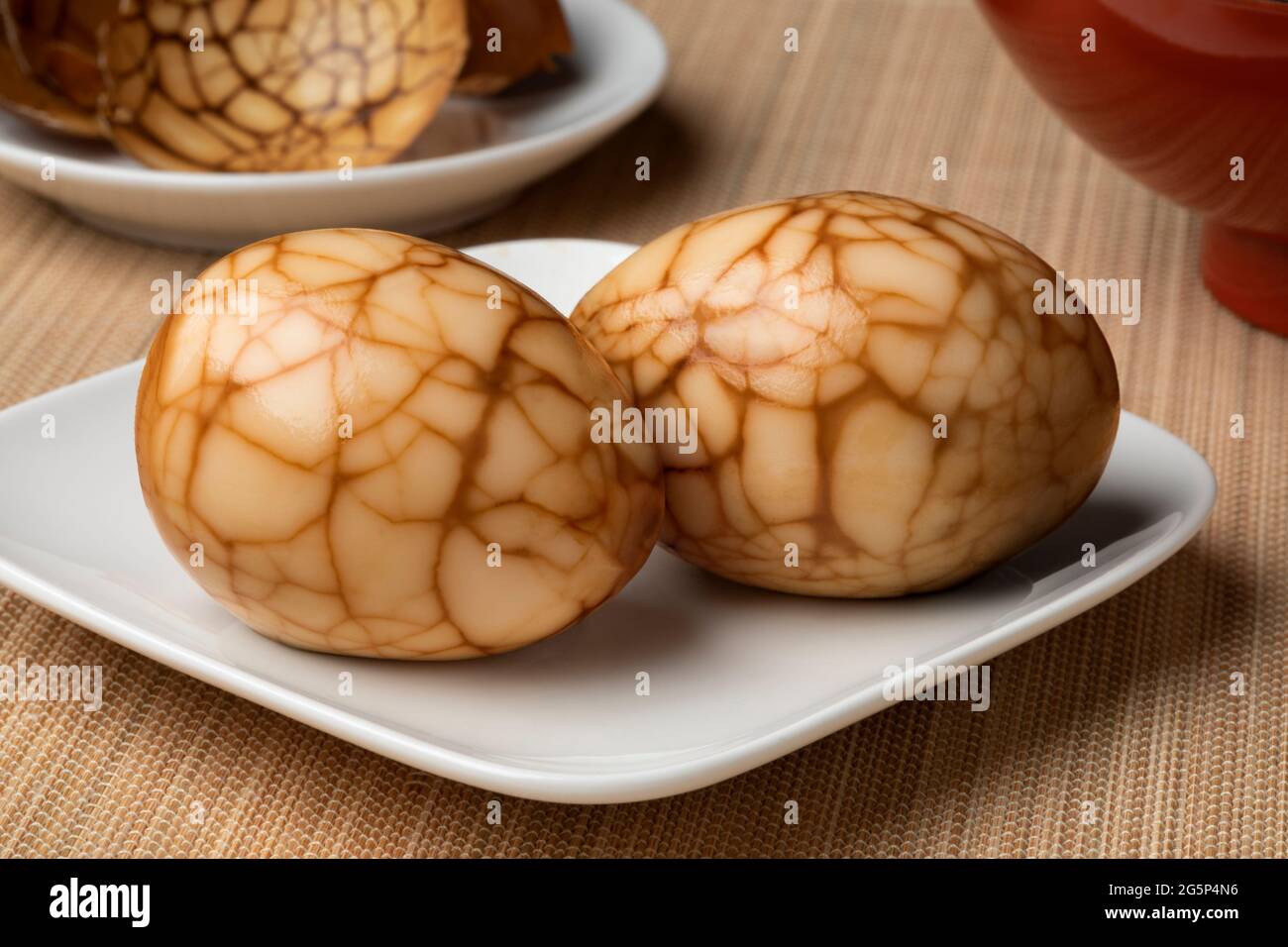 Ein Paar traditionelle chinesische Kräutertee-Eier auf einem Teller als Snack-Lebensmittel aus der Nähe und Eierschale im Hintergrund Stockfoto