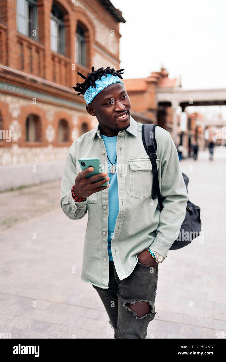 Schöner und cooler afrikanischer Mann, der auf der Straße läuft und sein Handy benutzt. Stockfoto