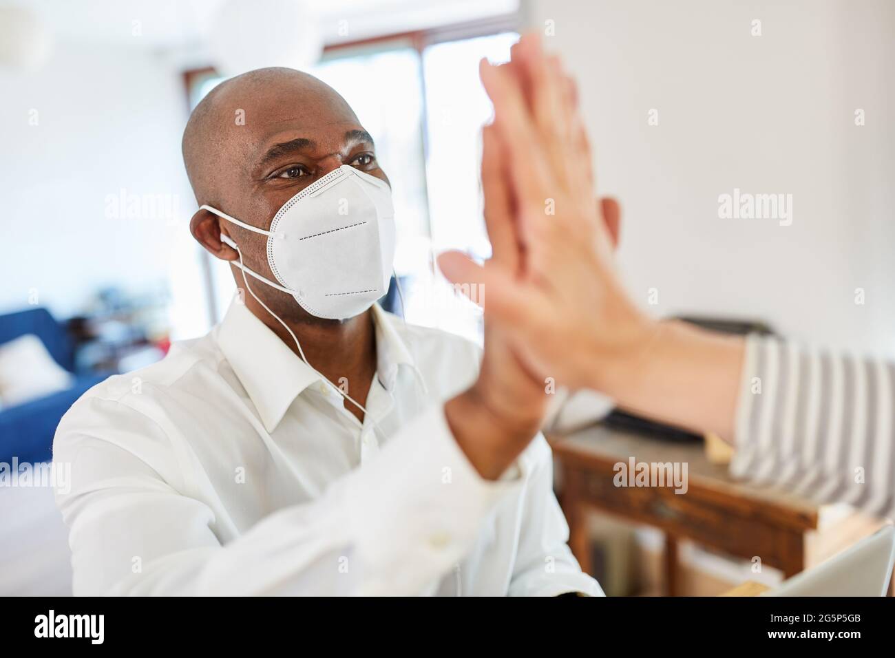 Geschäftsmann mit Maske wegen Covid-19 und Coronavirus mit den hohen fünf als Infektionsrisiko Stockfoto