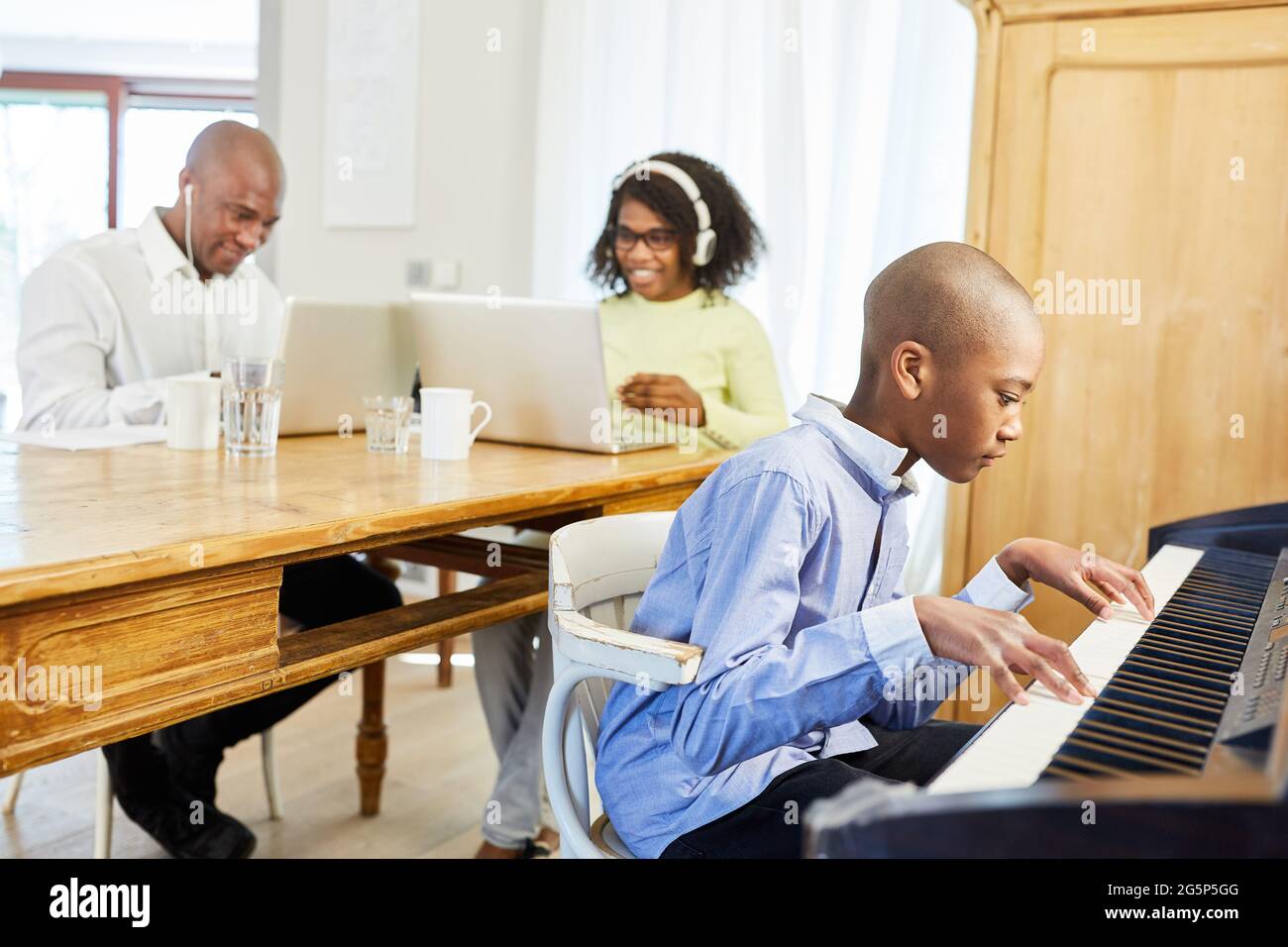 Afroamerikanische Familie, die von zu Hause aus arbeitet, mit Kind, das Klavier spielt Stockfoto