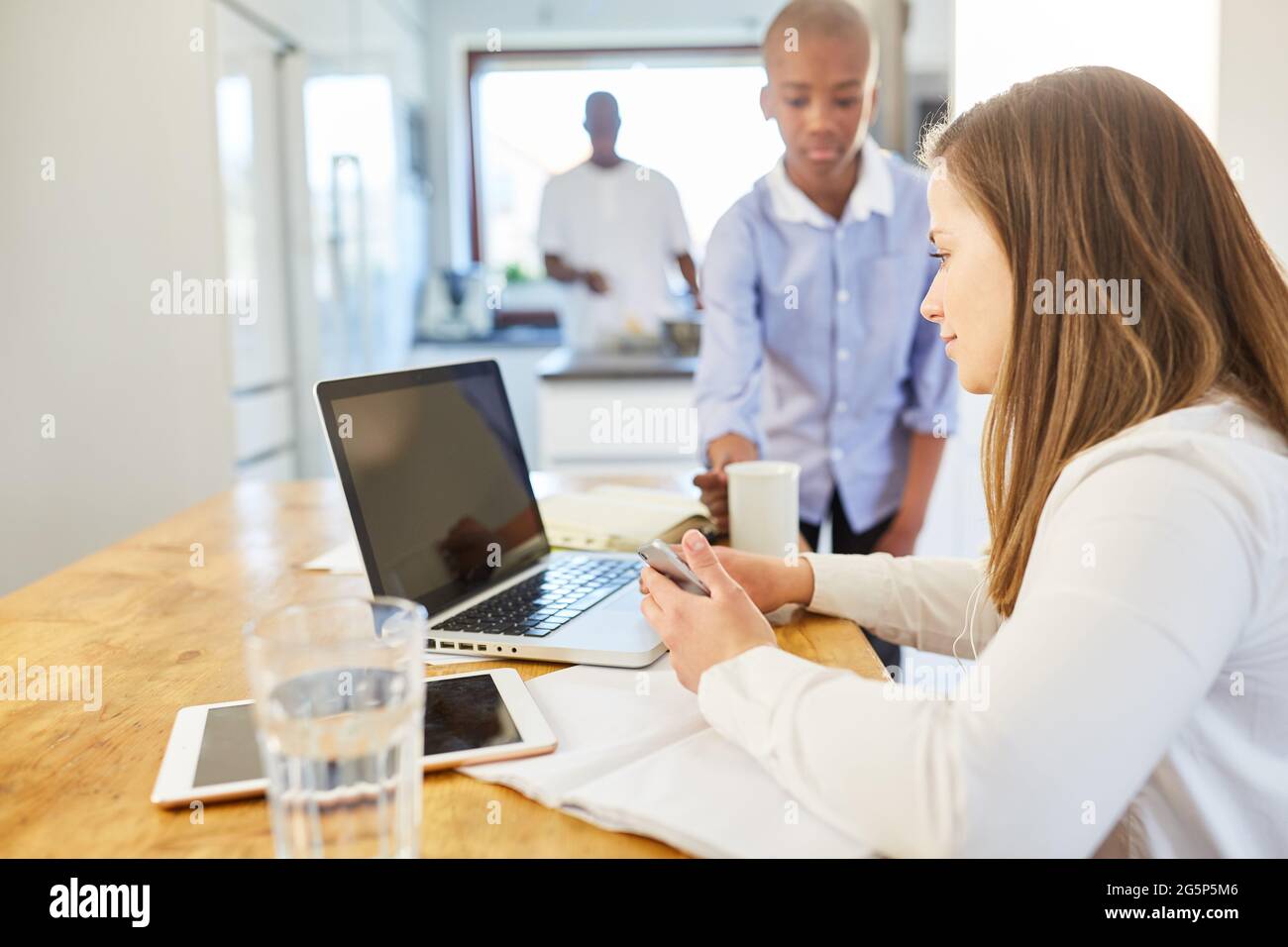 Das Kind bringt seiner Mutter eine Tasse Kaffee auf einem Laptop-PC online im Wohnzimmer als Heimbüro mit Stockfoto