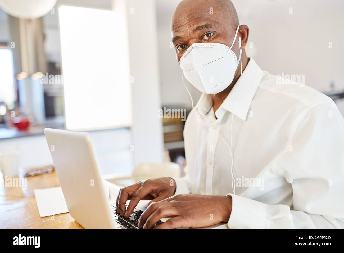 Afroamerikanischer Geschäftsmann mit Mund- und Nasenschutz wegen Covid-19 auf dem Laptop Stockfoto