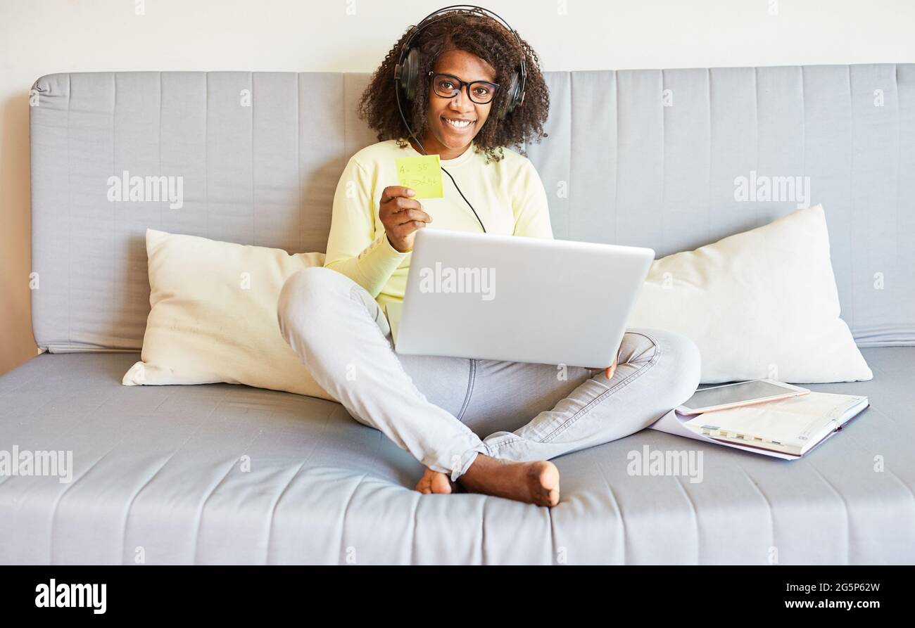 Afrikanische Frau, die zu Hause im Heimbüro mit einem Laptop und Kopfhörern auf dem Sofa arbeitet Stockfoto