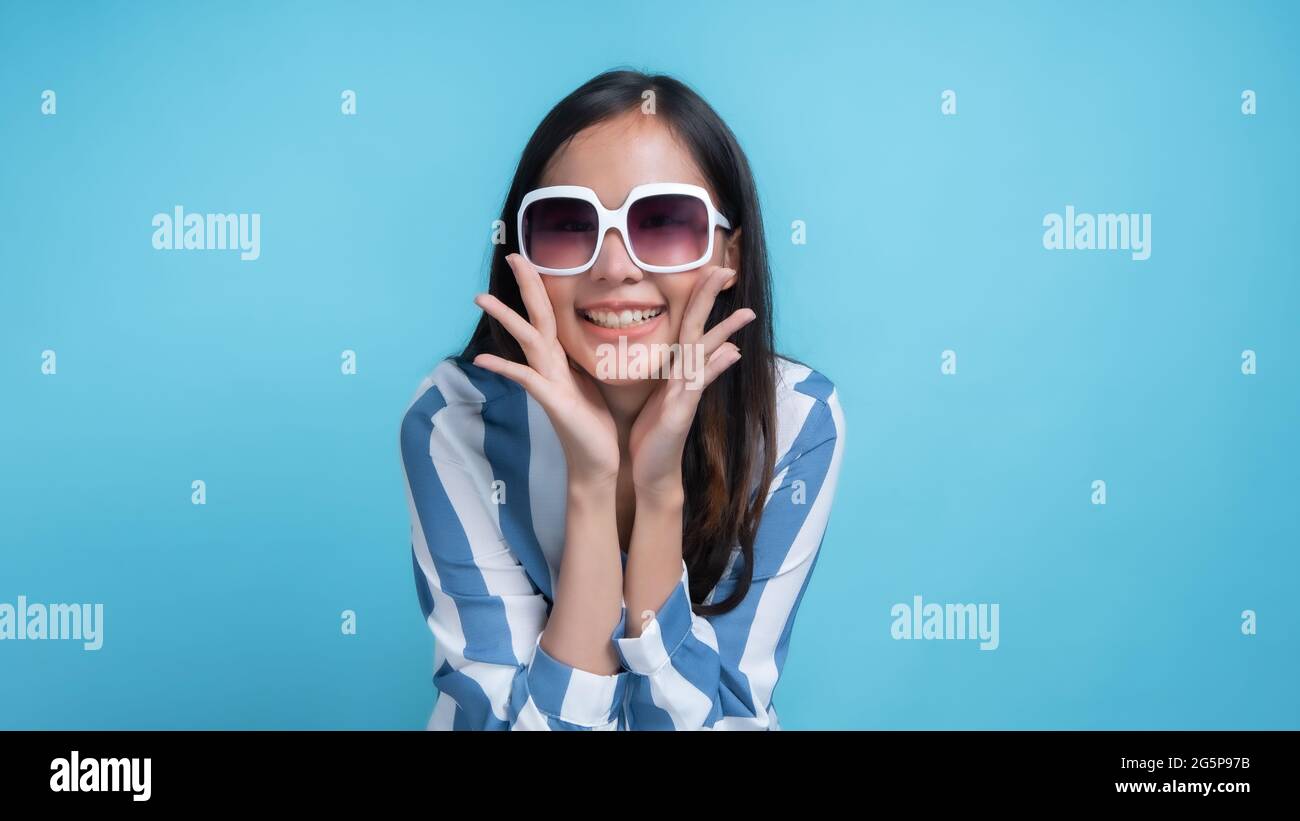 Aufgeregt junge asiatische Frau in weißen Gläsern schrie und lächelte mit Händen rund um den Mund isoliert auf blauem Hintergrund geschmunzelt Stockfoto