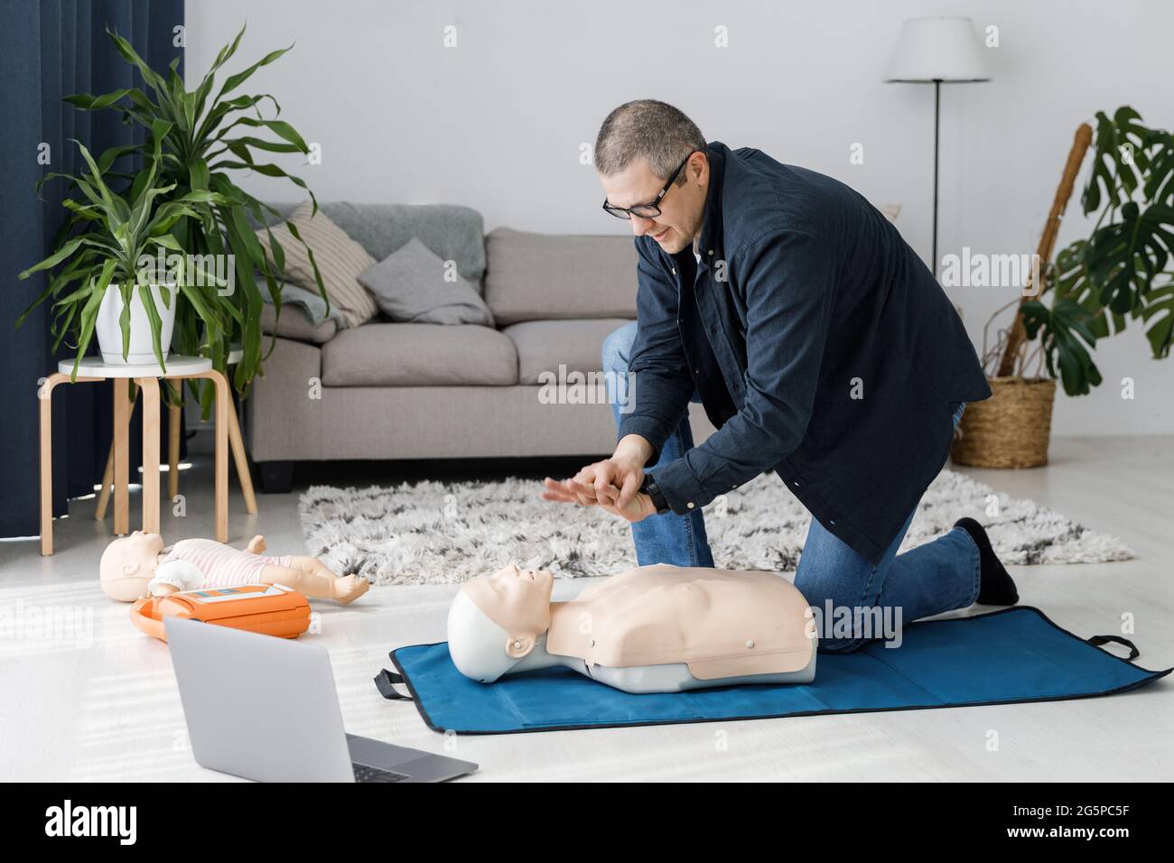 Sanitäter demonstrieren erste Hilfe an Übungspuppe während des Trainings allein im Wohnzimmer. Der Ausbilder zeigt die HLW an der Trainingspuppe Stockfoto