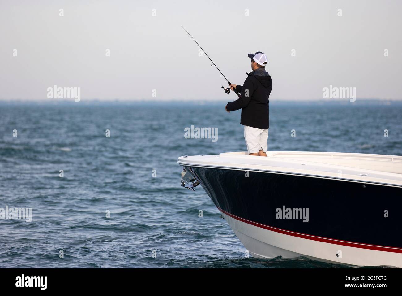 Mann, der aus dem Bug eines Bootes auf einem leeren See fischt. Stockfoto