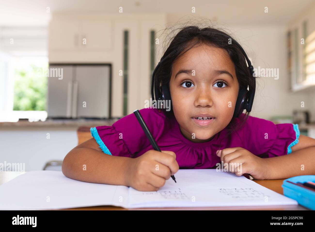 Glückliches hispanische Mädchen trägt Kopfhörer hören und schreiben während Online-Schulunterricht Stockfoto