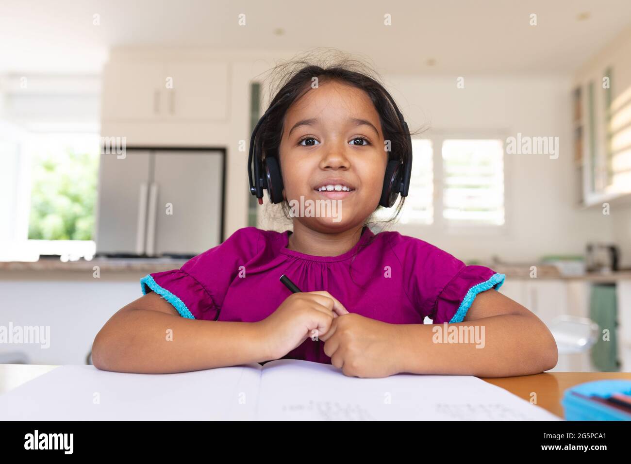 Glückliches hispanisch Mädchen trägt Kopfhörer lächelnd während der Online-Schulstunde Stockfoto