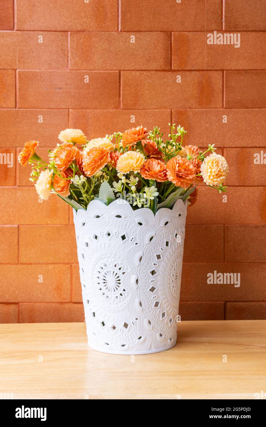 Mockup Blume auf einem Holztisch mit einem Backstein Wand orange Hintergrund. Stockfoto