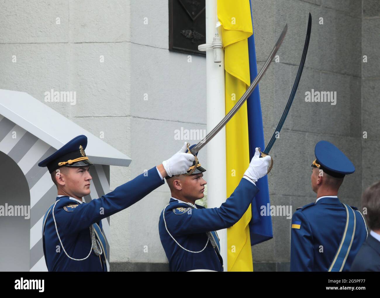 KIEW, UKRAINE - 28. JUNI 2021 - Ehrengarde halten Säbel aus, während sie die Nationalflagge vor dem Gebäude der Verfassung von Werchowna Rada hochheben Stockfoto