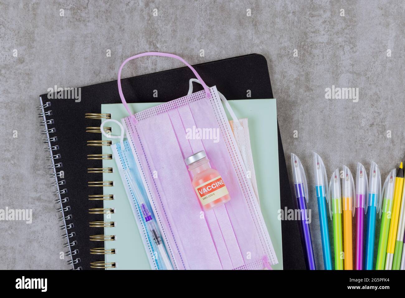 Schulbedarf auf einer Vielzahl von farbigen Papeterie im Rücken zur Schule in medizinischen Masken auf dem Covid-19-Coronavirus Stockfoto