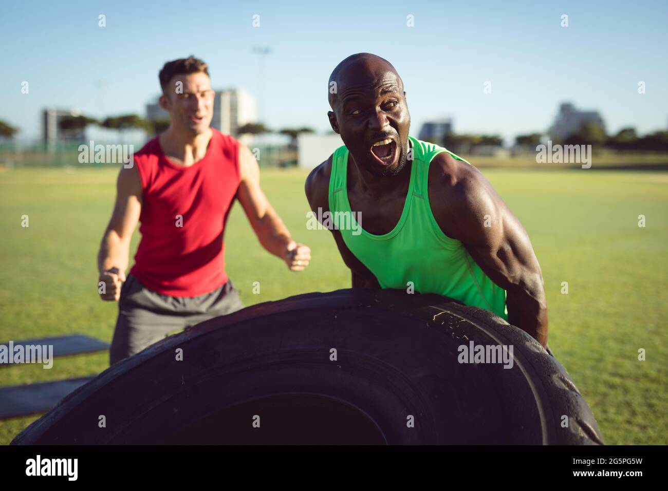 Diverse fit Mann und Trainer trainieren im Freien, fördern und heben schwere Reifen Stockfoto
