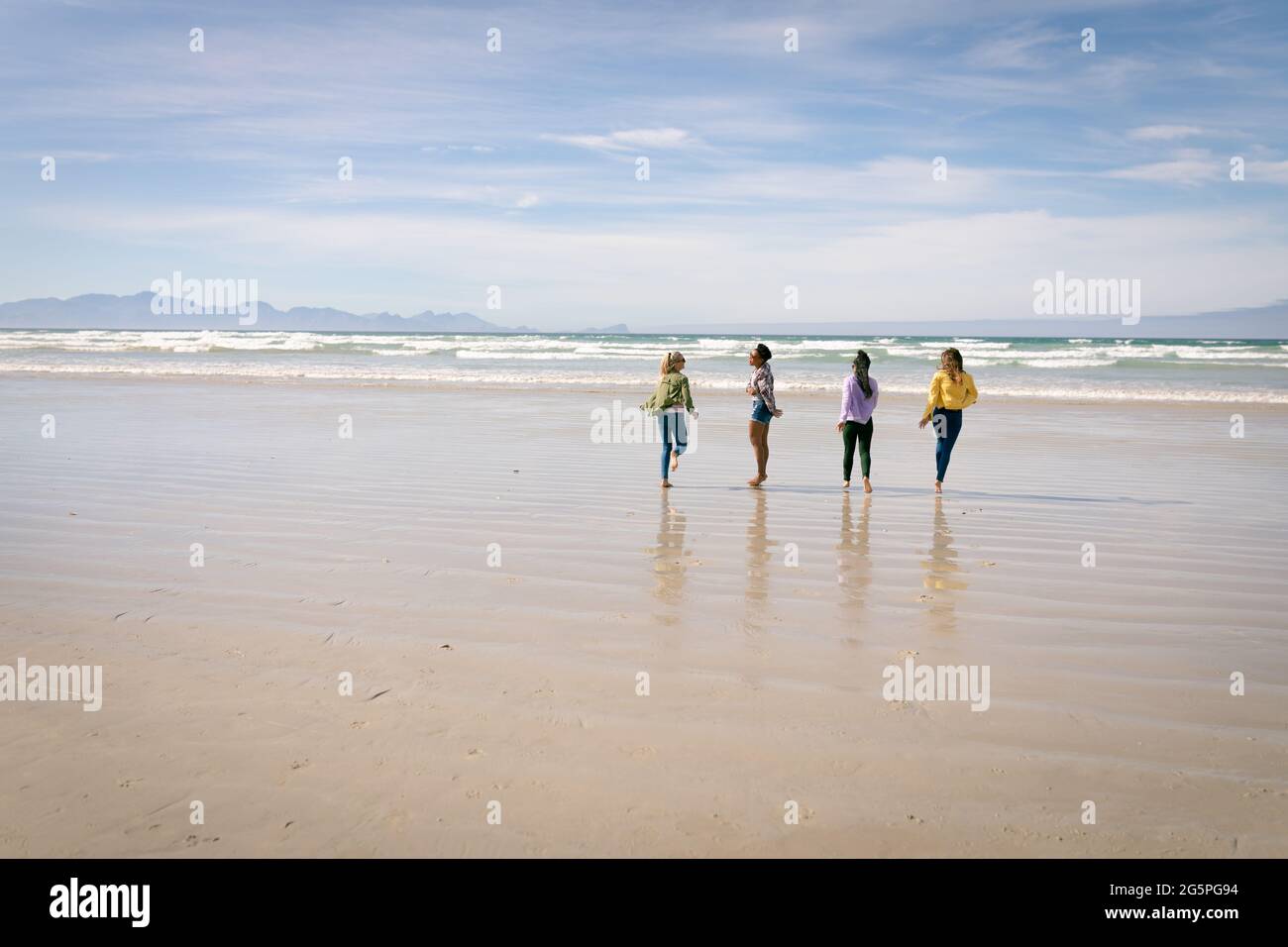 Fröhliche Gruppe verschiedener Freundinnen, die Spaß haben, am Strand entlang spazieren und lachen Stockfoto