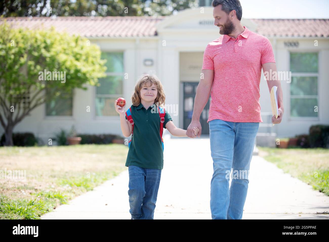 Glückliche Familie von Kind und Vater mit Apfel halten Hände, was zur ersten Schulstufe, Schule Stockfoto