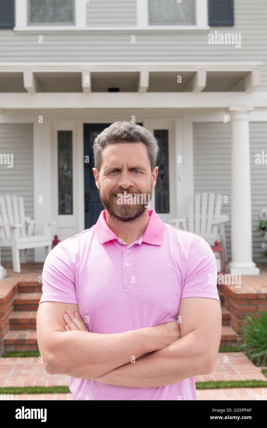 Glücklicher bärtiger Mann in der Nähe eines neuen Hauses nach der Miete oder dem Kauf eines neuen Hauses, einer Immobilie Stockfoto