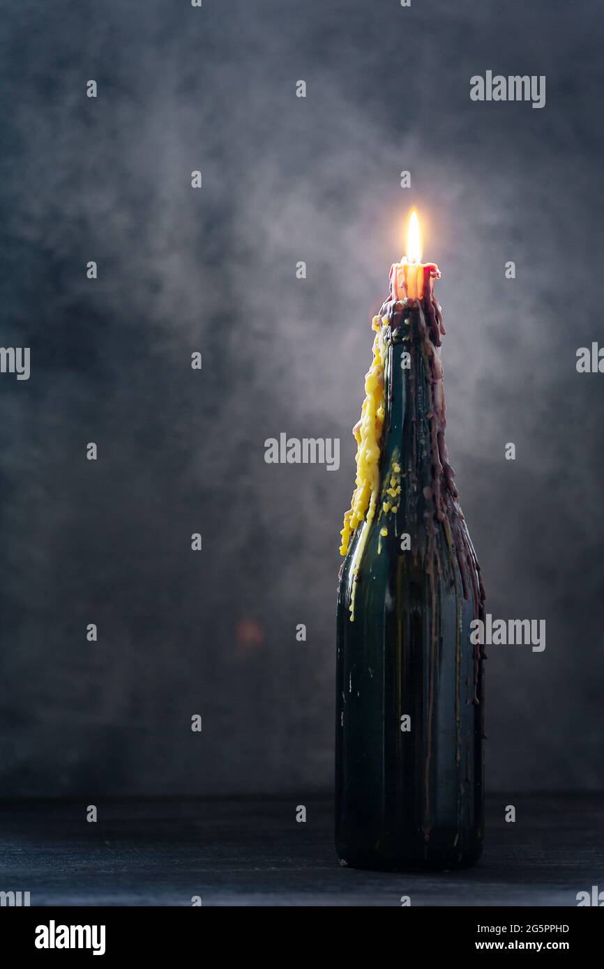 Brennende Kerze mit geschmolzenem Wachs in einer Flasche auf dunklem Hintergrund, halloween-Dekoration mit mystischem Licht Stockfoto