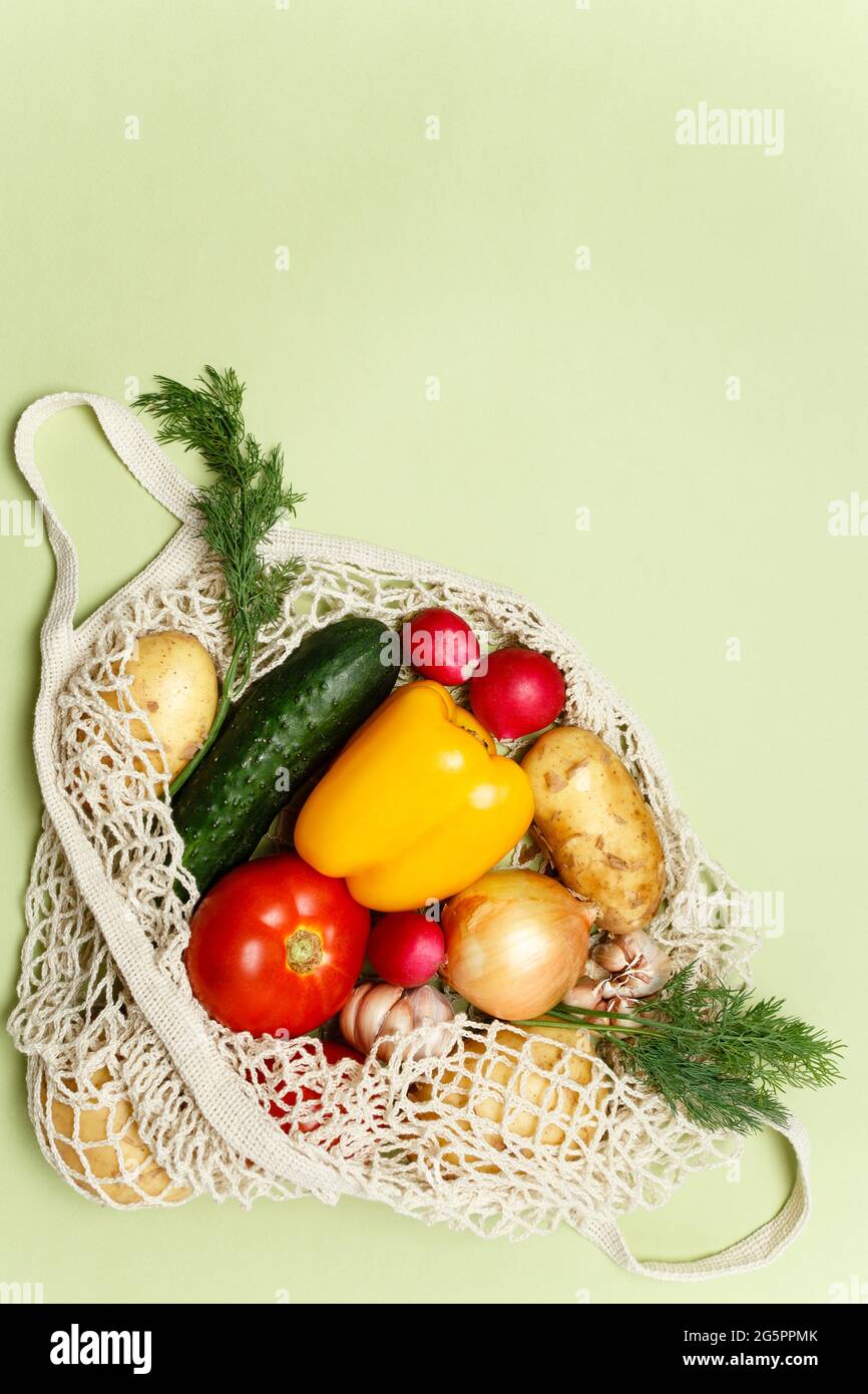 Trendiger Saitenbeutel mit frischem Gemüse und Gemüse auf hellgrünem Hintergrund: Kartoffeln, Tomaten, Zwiebel, Paprika. Zero Waste Sustainable Livesty Stockfoto
