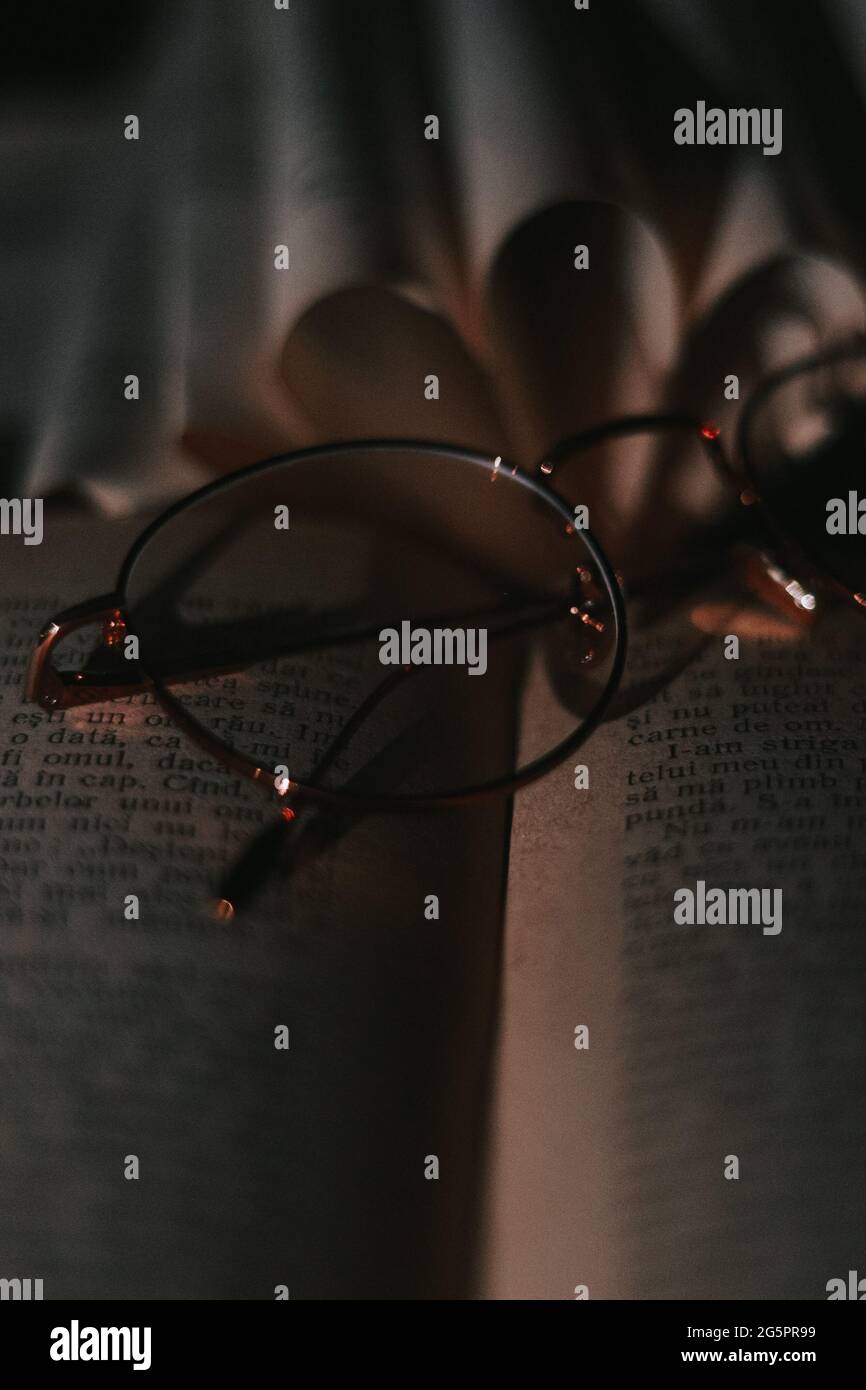 Dark Cinematic Nahaufnahme von braunen Goldgläsern mit einem Buch im Hintergrund und unter der Brille. Dieses Bild ist inspirierend und motivierend Stockfoto
