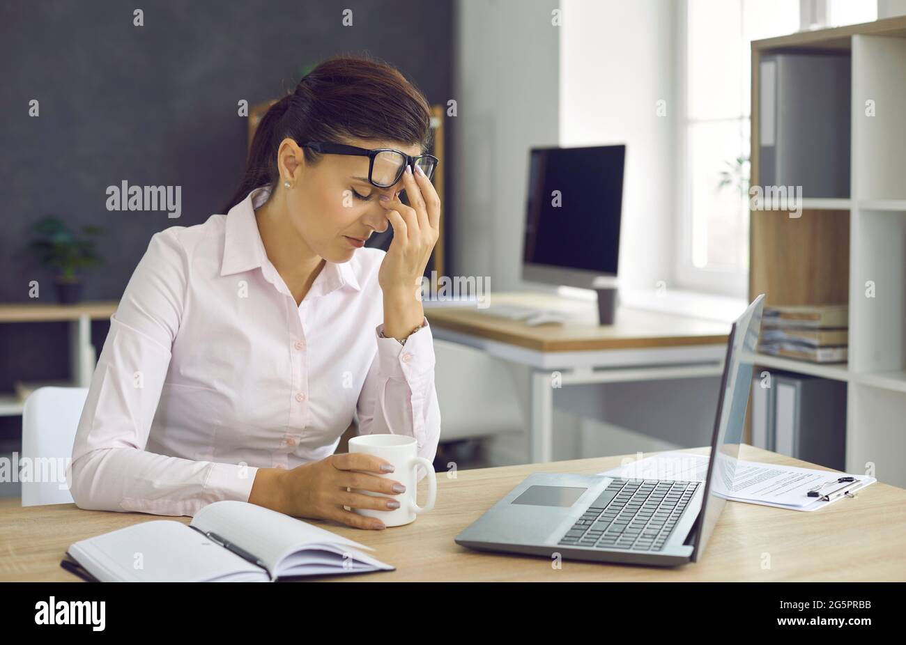 Junge, müde Frau, die sich während einer Pause von der Büroarbeit ausruhte und ihre Brille aufhob Stockfoto