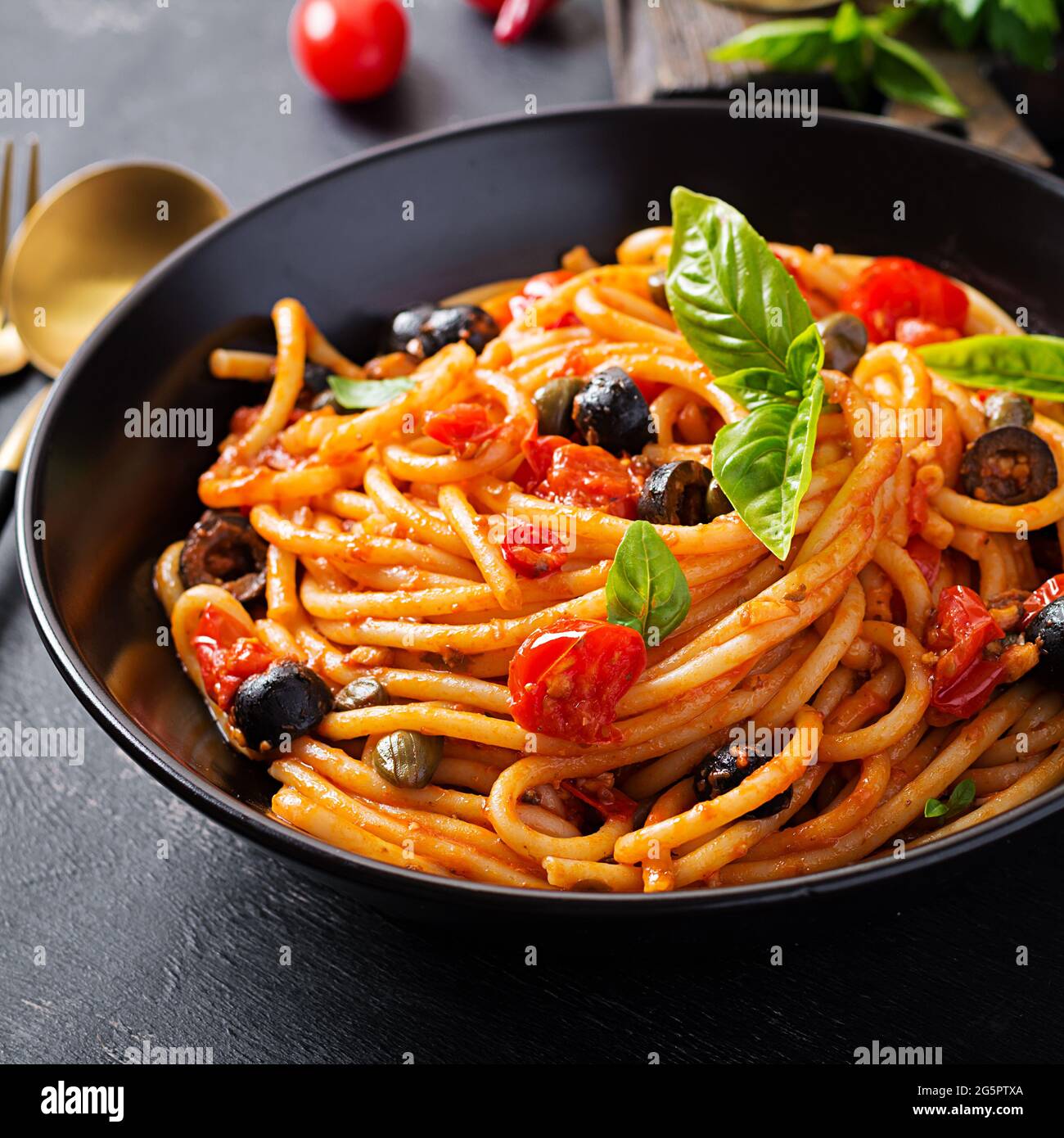 Spaghetti alla puttanesca – italienische Pasta-Gericht mit Tomaten, schwarzen Oliven, Kapern, Sardellen und Basilikum. Stockfoto