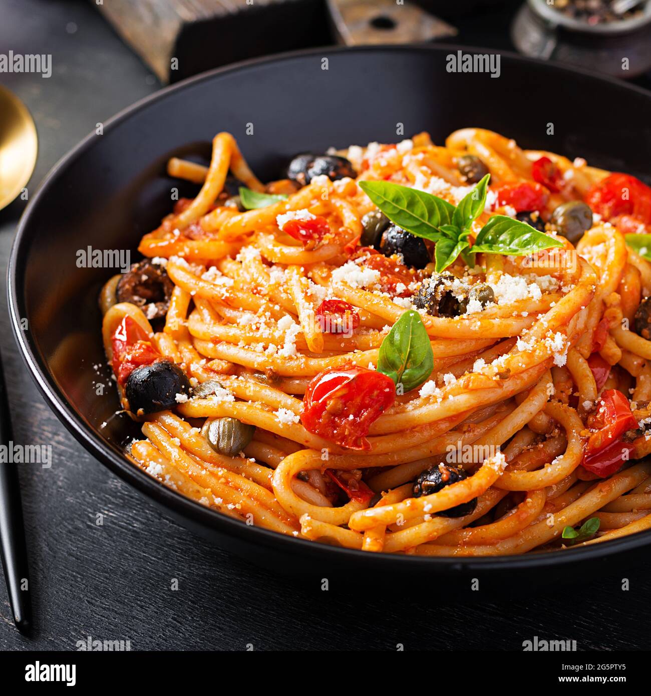Spaghetti alla puttanesca – italienische Pasta-Gericht mit Tomaten, schwarzen Oliven, Kapern, Sardellen und Basilikum Stockfoto