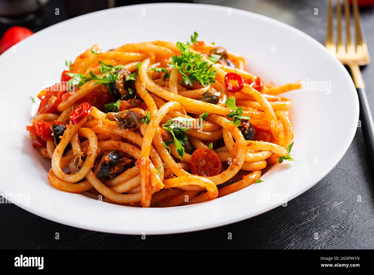 Spaghetti alla Puttanesca – italienisches Nudelgericht mit Tomaten, schwarzen Oliven, Kapern, Sardellen und Petersilie. Stockfoto