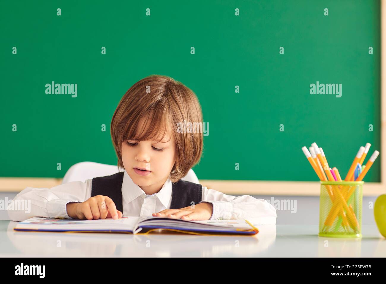 Zurück zur Schule. Ein Schüler liest ein Buch, während er an einem Tisch in einem Klassenzimmer sitzt. Stockfoto