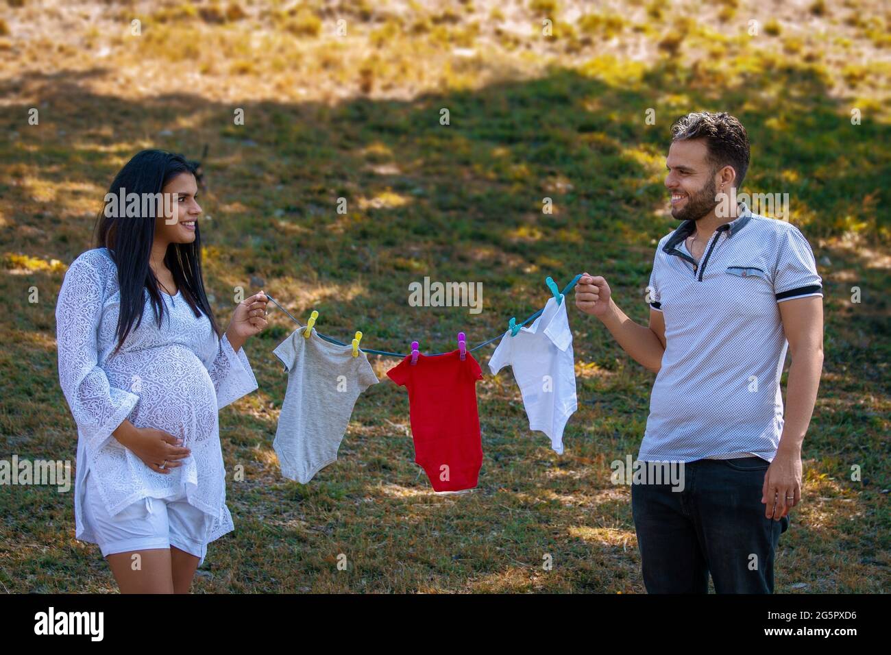 Junges Paar mit einem Garn und hängender Babykleidung. Die junge Frau ist schwanger Stockfoto