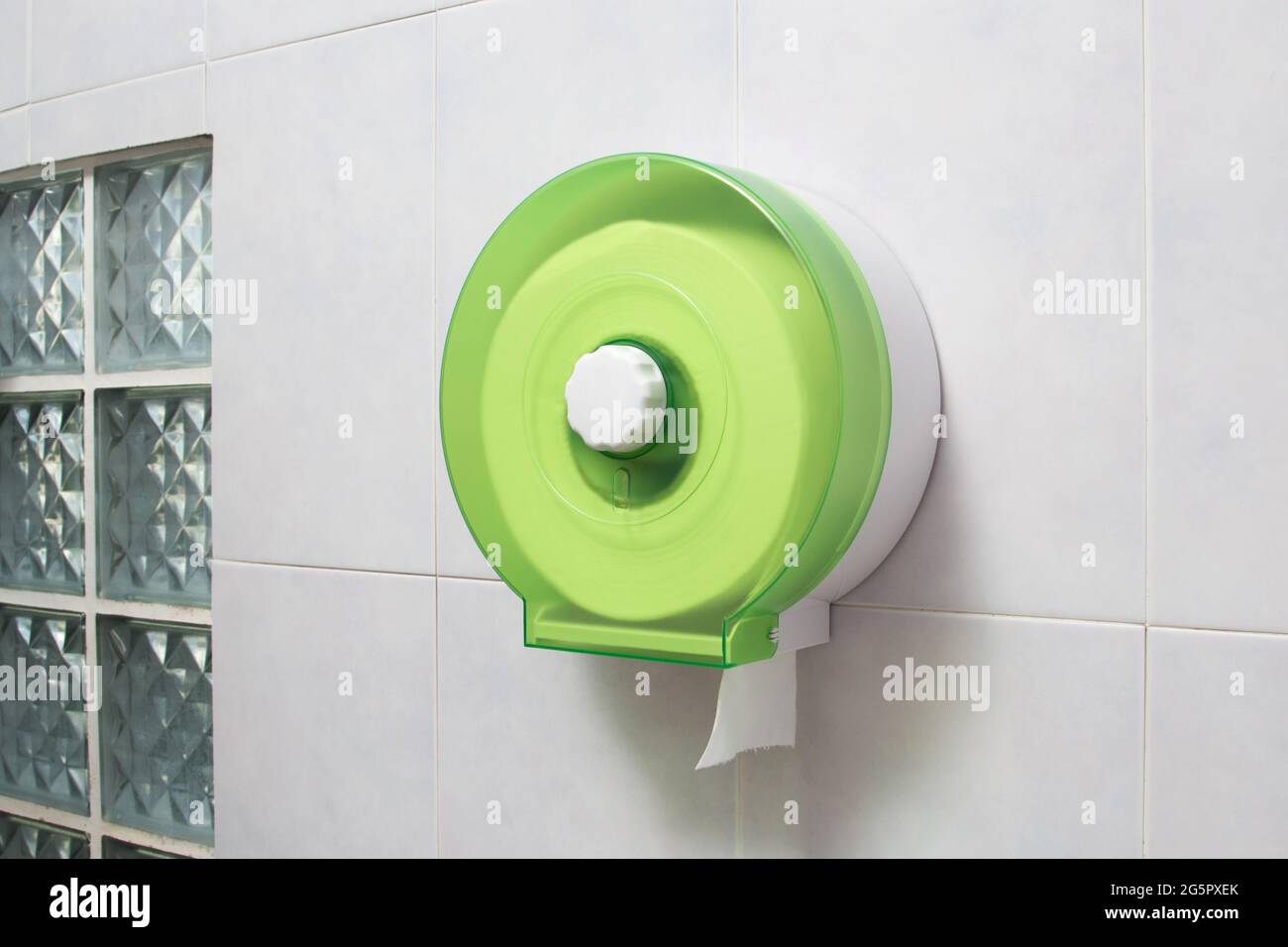 Grüner Toilettenpapierrollenhalter aus Kunststoff mit weißem Seidenpapier an der Fliesenwand im Badezimmer Stockfoto