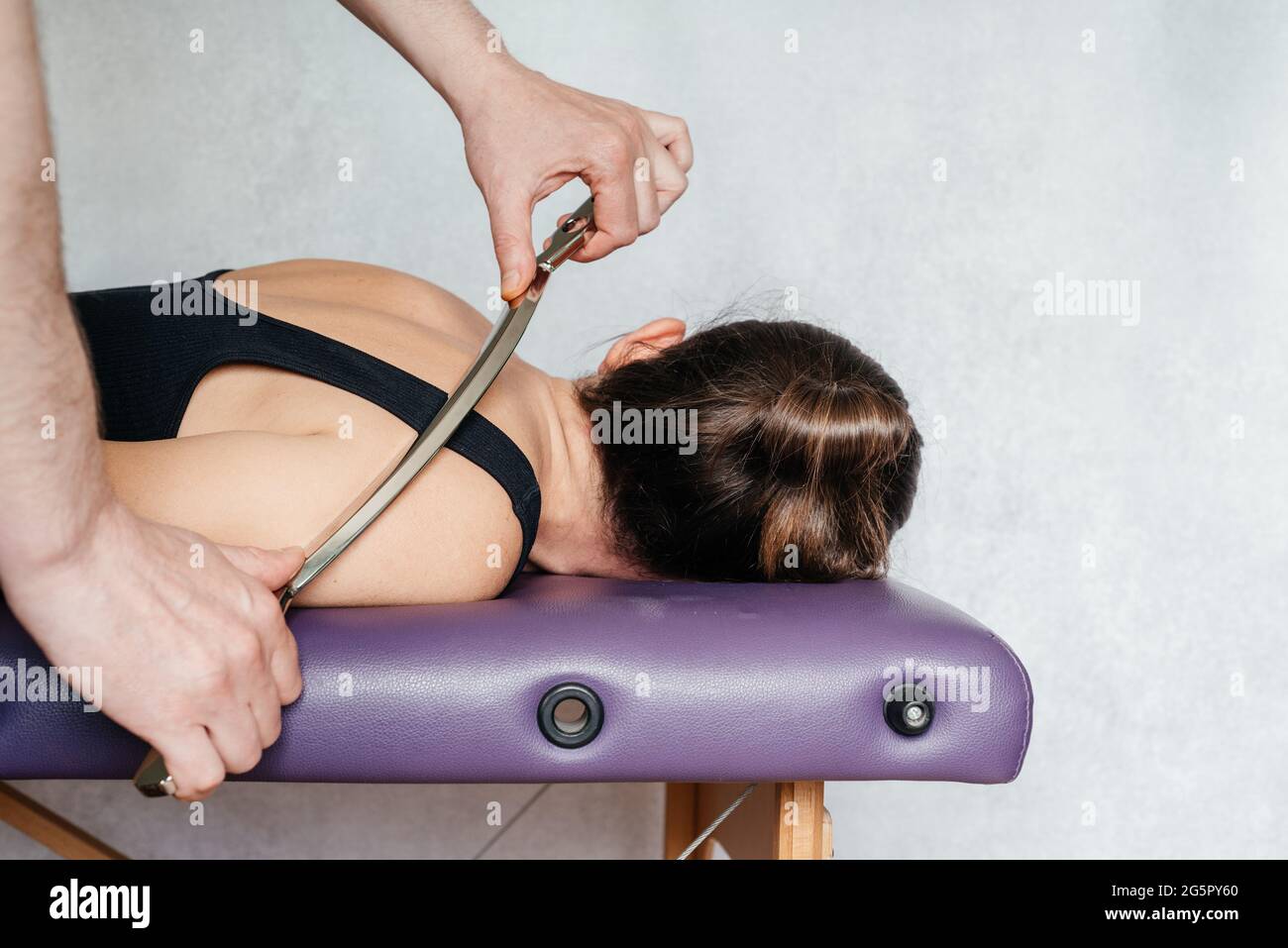 IASTM-Behandlung bei myofaszialer Einschränkung, einer Frau, die eine Weichteilbehandlung am Hals mit dem IASTM-Werkzeug aus Edelstahl erhält Stockfoto