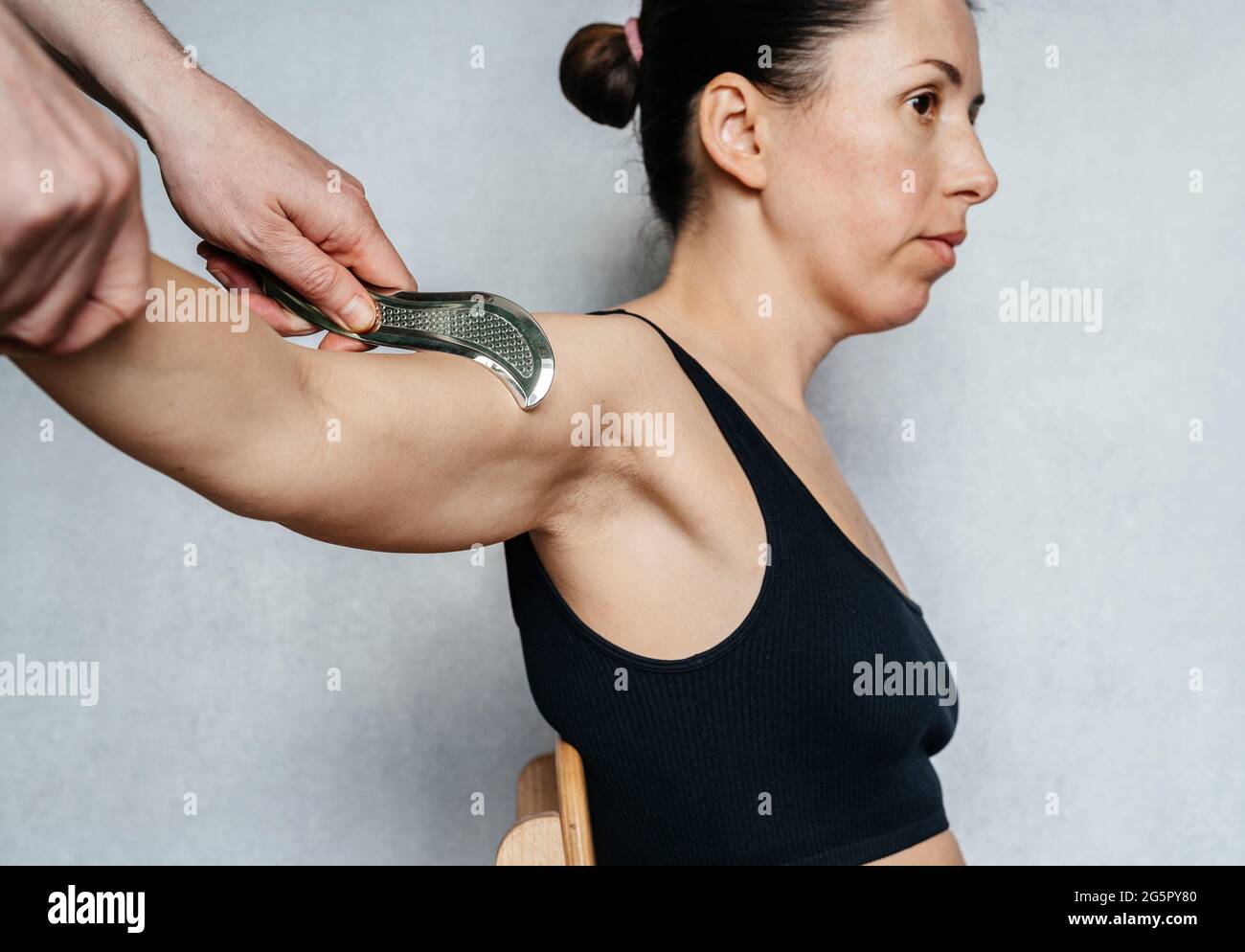 IASTM-Behandlung für myofasziale Einschränkung, eine Frau, die eine Weichteilbehandlung an ihrem Arm mit dem guasha IASTM Edelstahlwerkzeug erhält Stockfoto