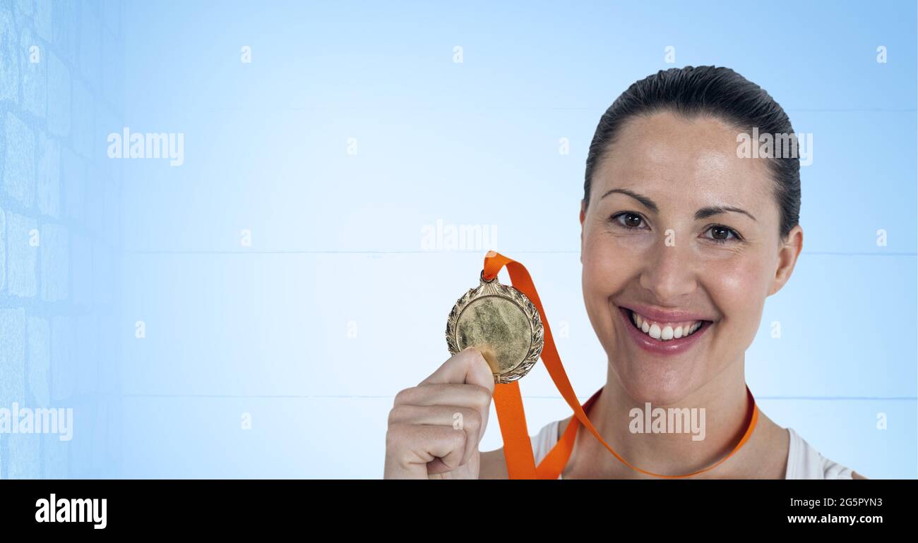 Porträt einer kaukasischen Athletin, die eine Medaille um den Hals hält und vor blauem Hintergrund lächelt Stockfoto