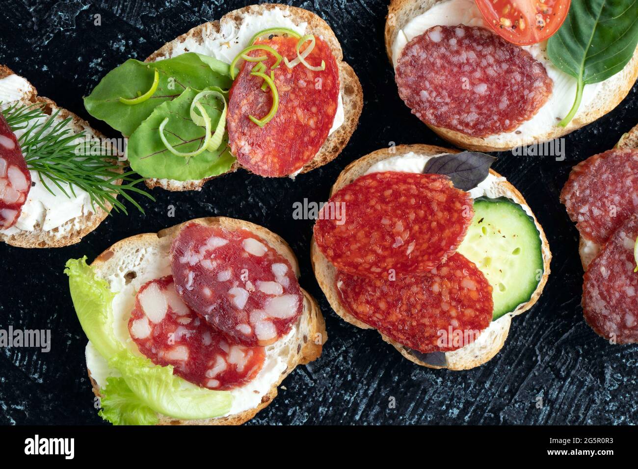 Nahaufnahme von Sandwiches oder Snacks mit verschiedenen Würstchen und Gemüse auf schwarzem Hintergrund. Weicher Fokus. Draufsicht. Flach liegend Stockfoto
