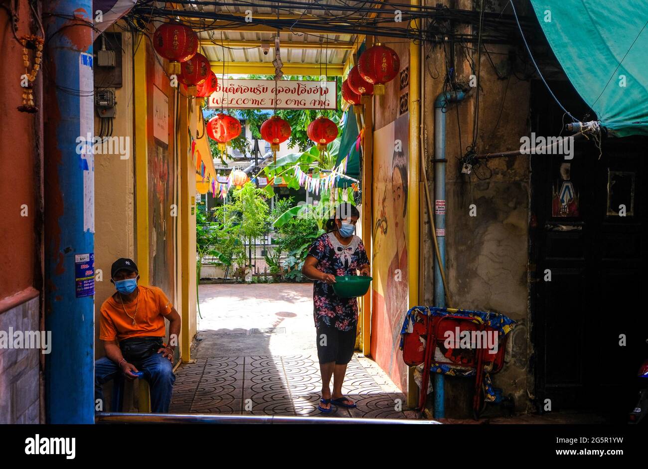 Die Menschen gehen in einer engen, sonnendurchfluteten Gasse in der Nähe von Klong Ong Ang in Bangkok, Thailand, ihren täglichen Geschäften nach Stockfoto